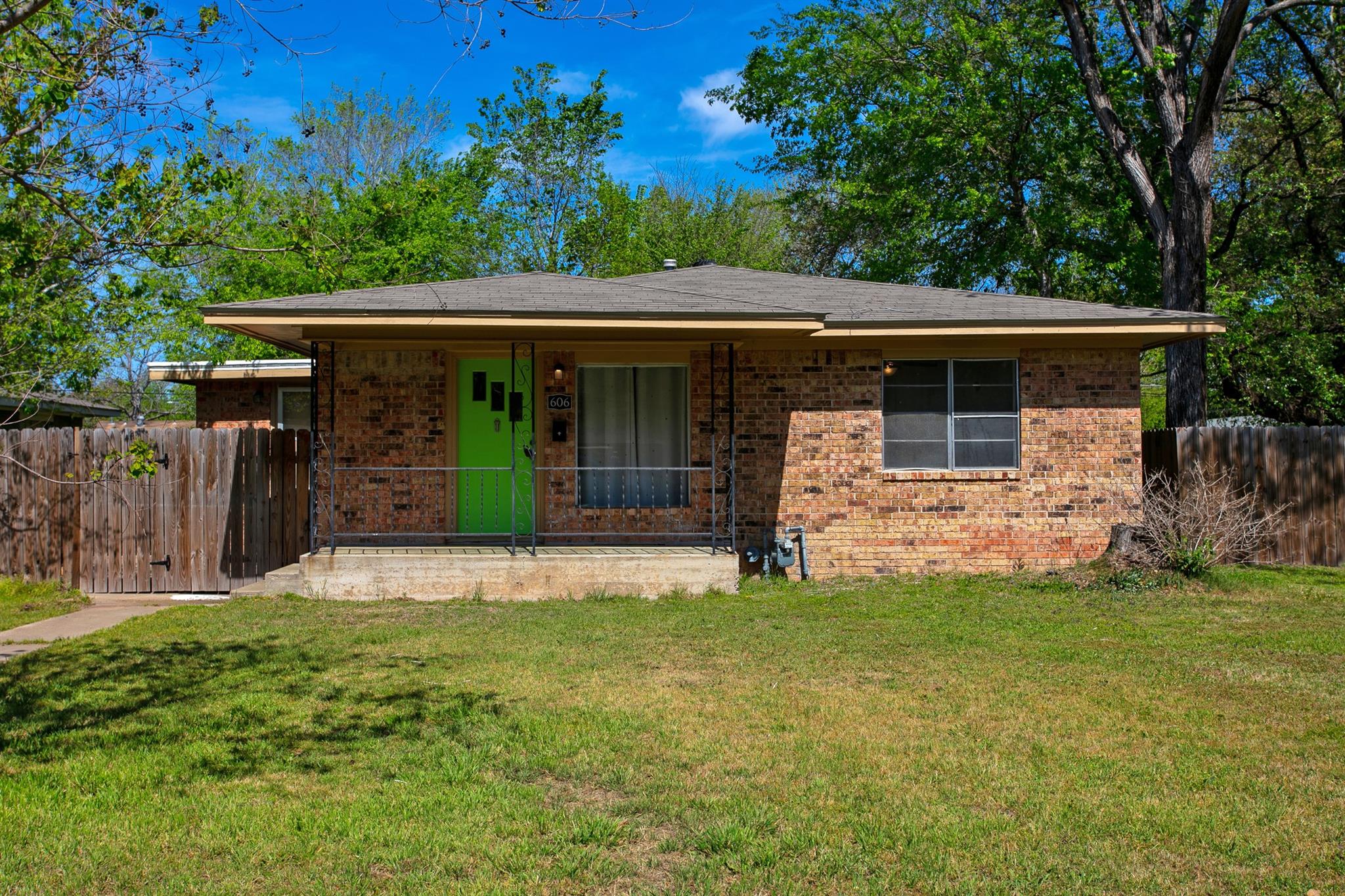 Single-story brick house with a bright green front door, covered porch, and fenced yard.