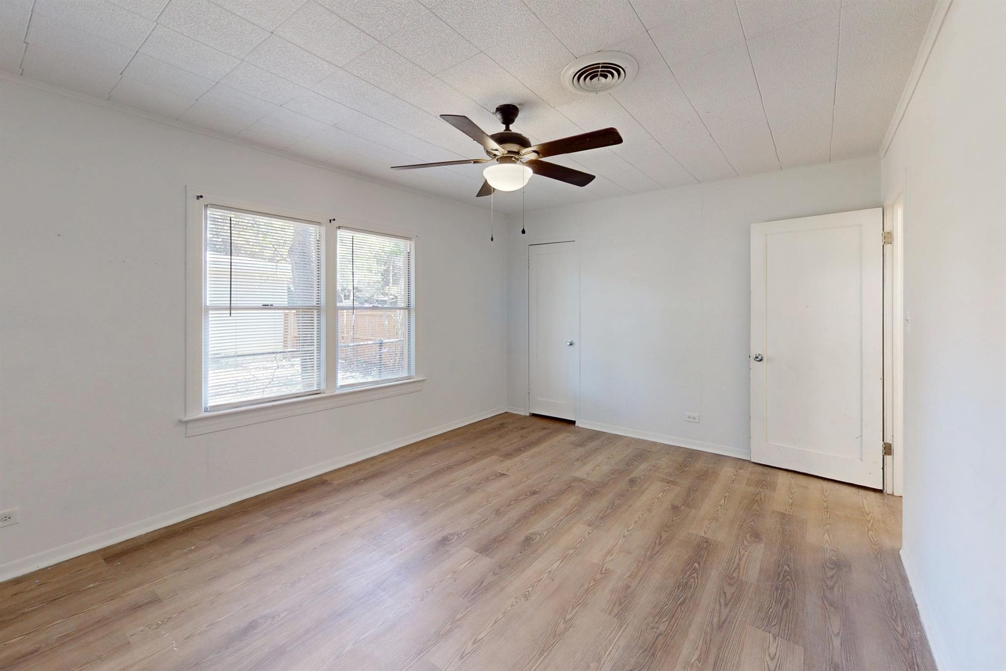 Empty room with wood-look floors, two windows, and a ceiling fan with light.