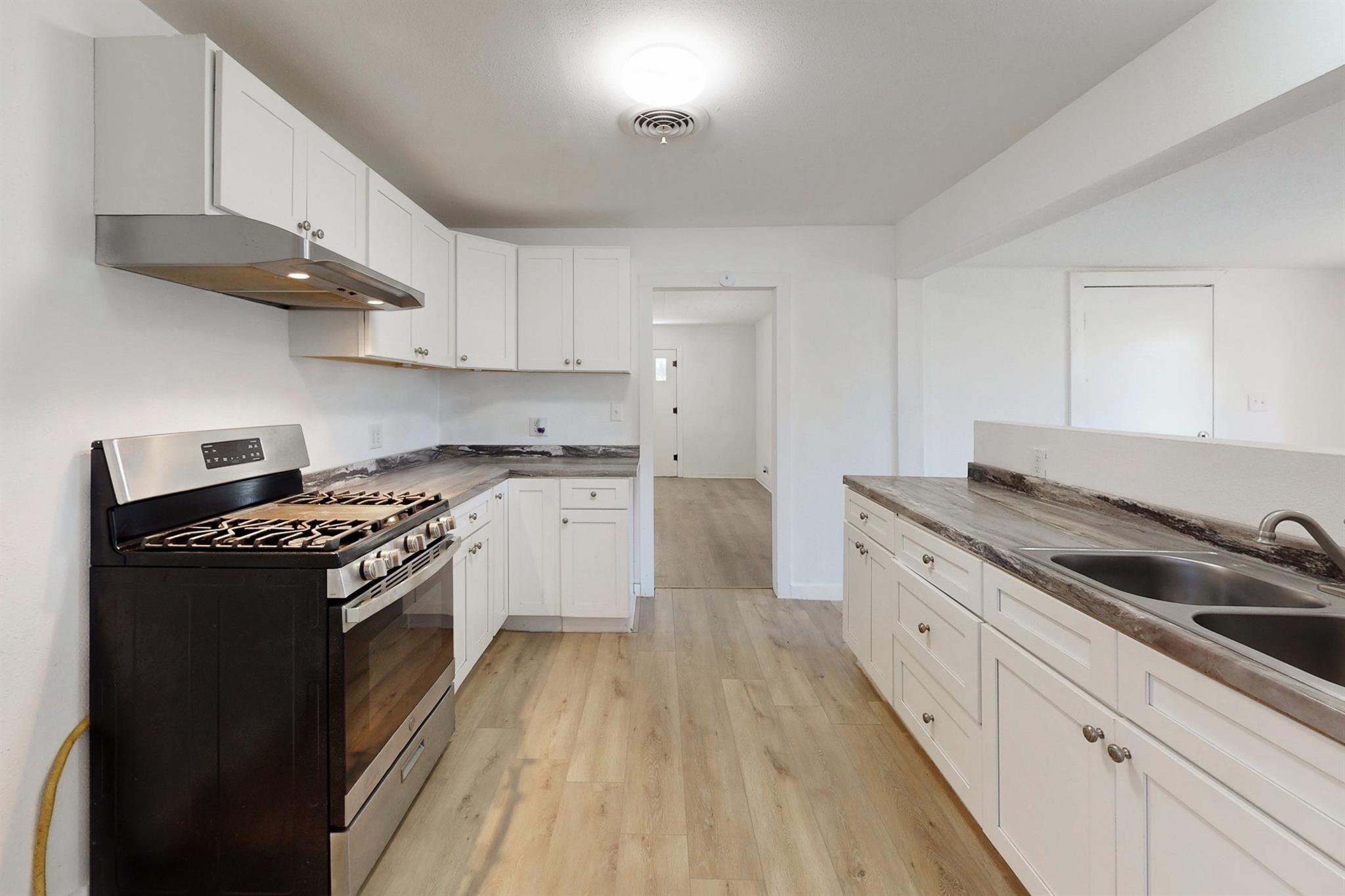 Kitchen with white cabinets, wood-look flooring, a black gas range, and a double-basin sink.