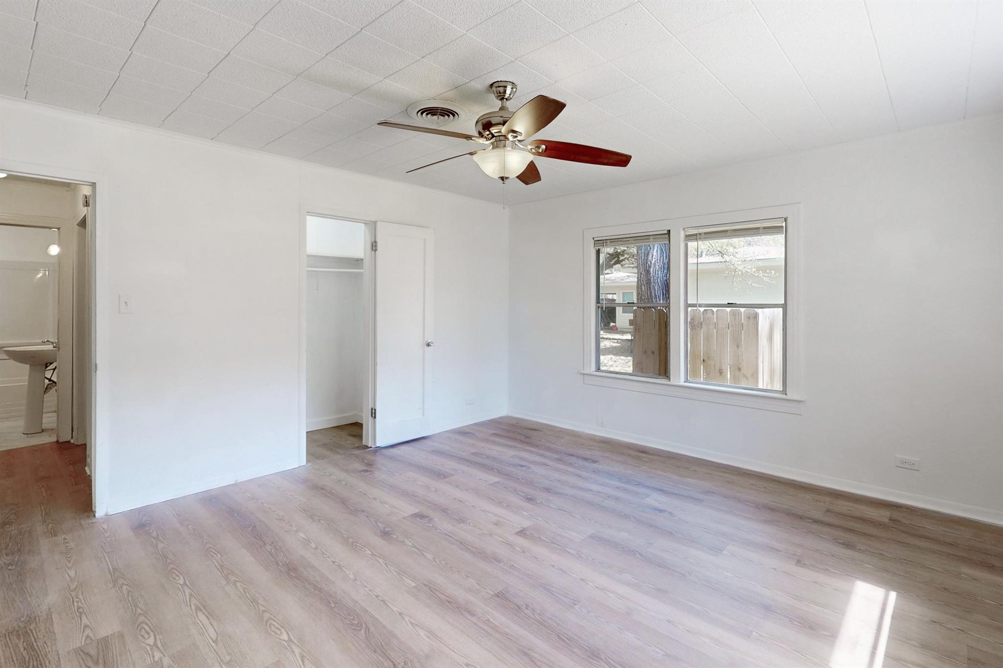 Empty bedroom with pale wood-look floors, ceiling fan, open closet, and two windows.