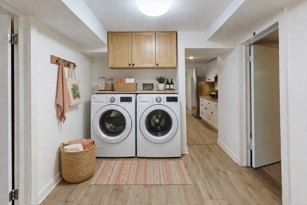 Laundry room with front-loading washer and dryer, light wood cabinets, and a striped rug.
