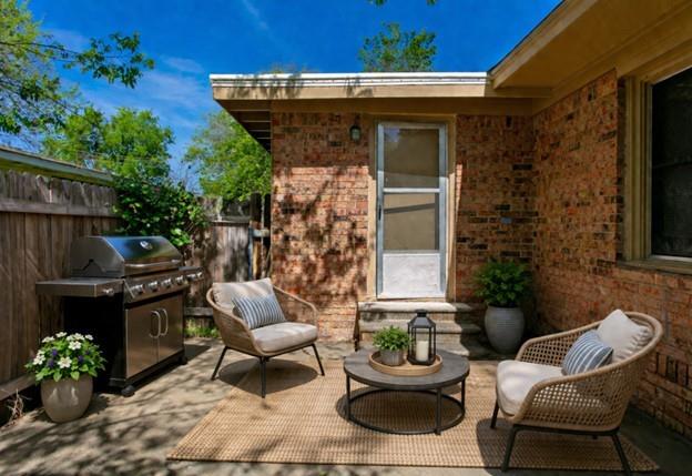 Brick patio with a barbecue grill, wicker seating, and a round coffee table beside the house.