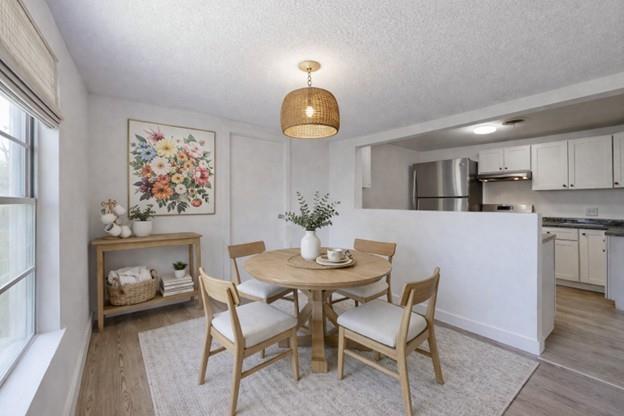 Dining area with a round wooden table, woven pendant light, and open kitchen.