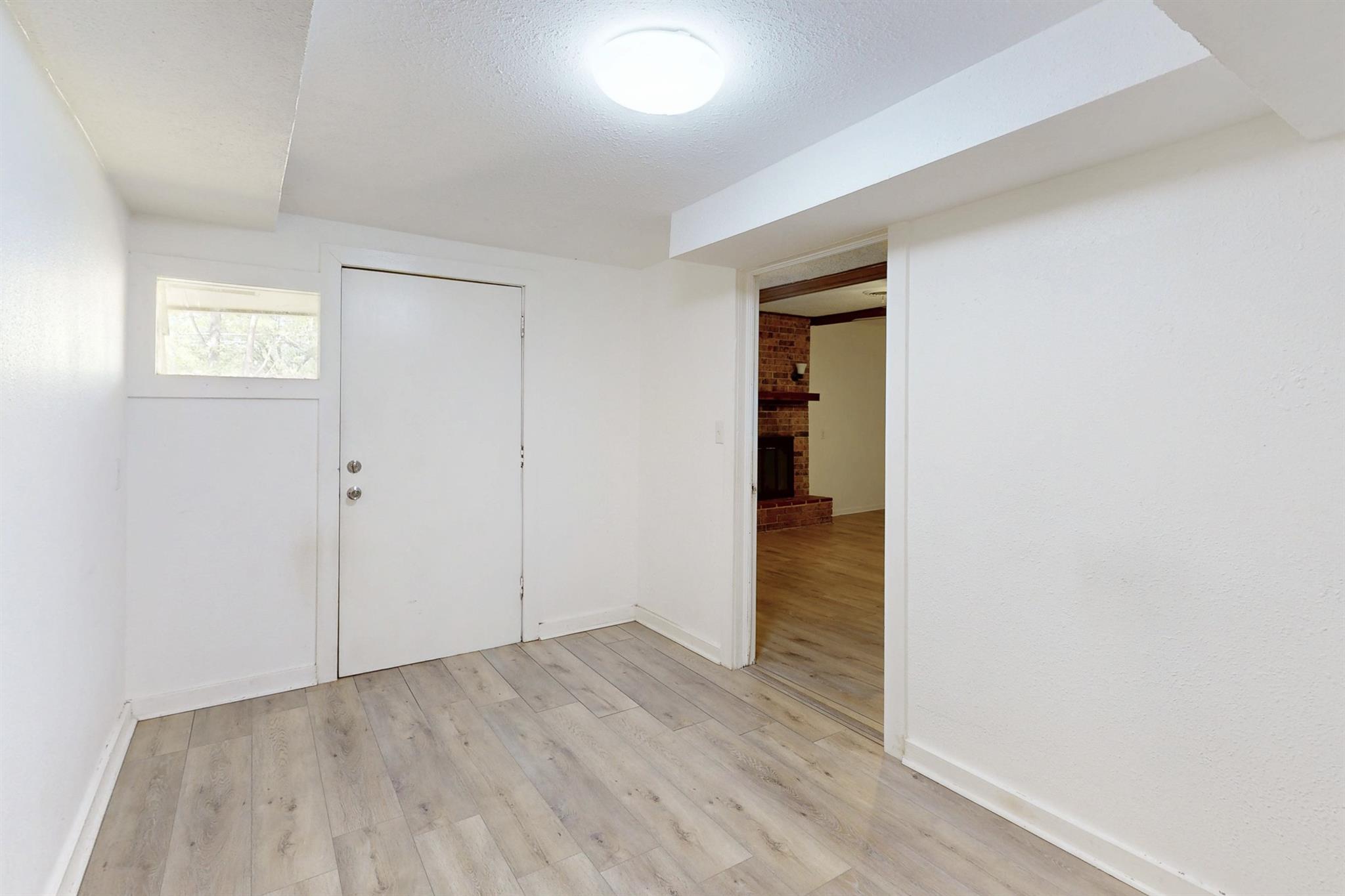 Entry foyer with pale plank flooring, a white front door, and a view of a brick fireplace.