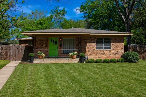 Single-story brick home with a bright green front door, potted plants, and a broad lawn.