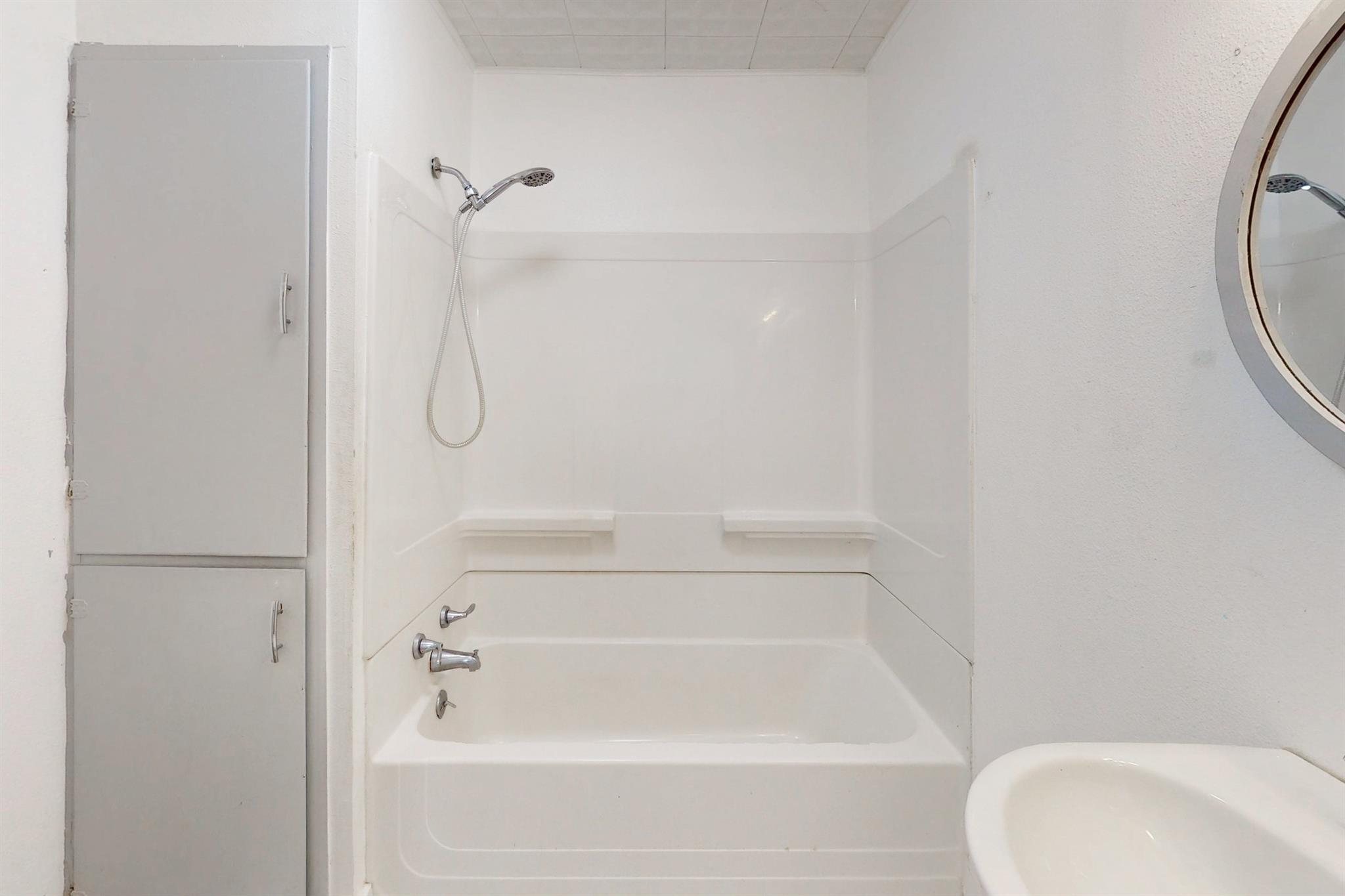 Bathroom with a white tub and shower, handheld showerhead, and built-in storage cabinets.