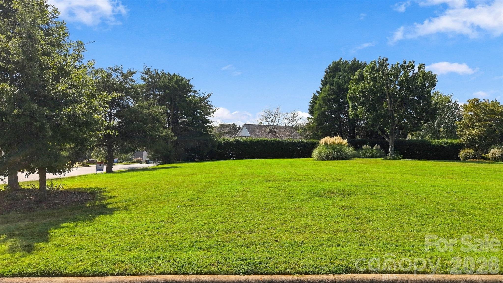 Broad green lawn bordered by mature trees and hedges, with a house partly visible behind them.