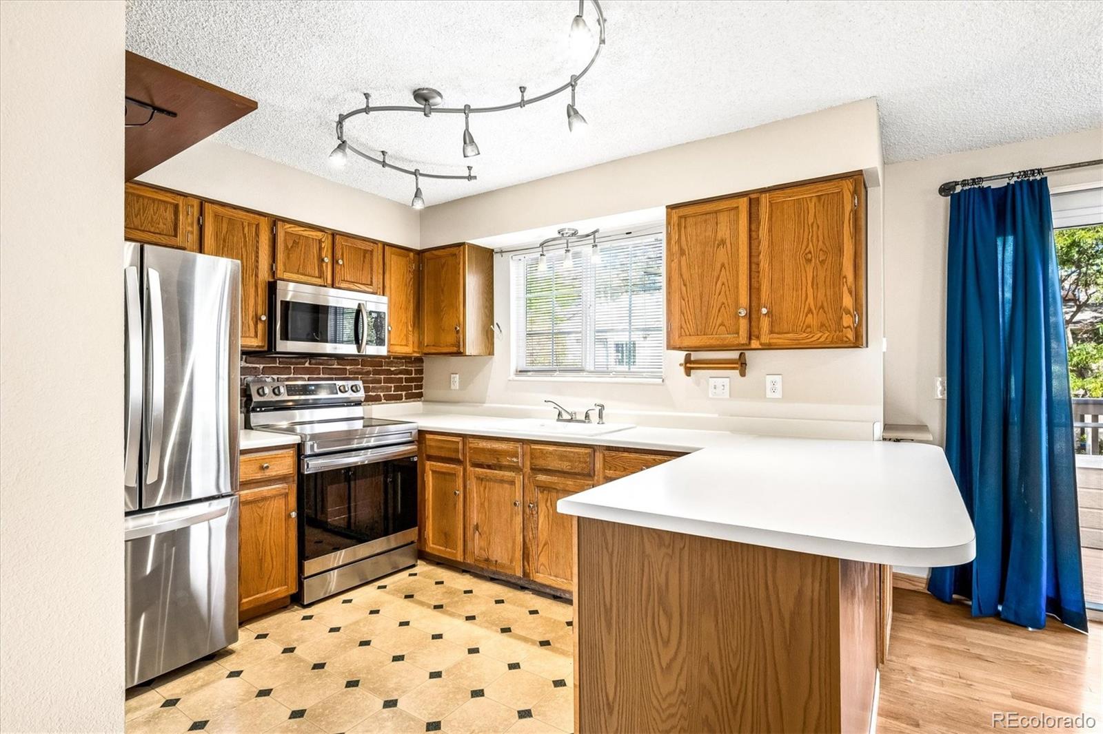 Kitchen with wood cabinets, stainless steel appliances, brick backsplash, and a large white peninsula.