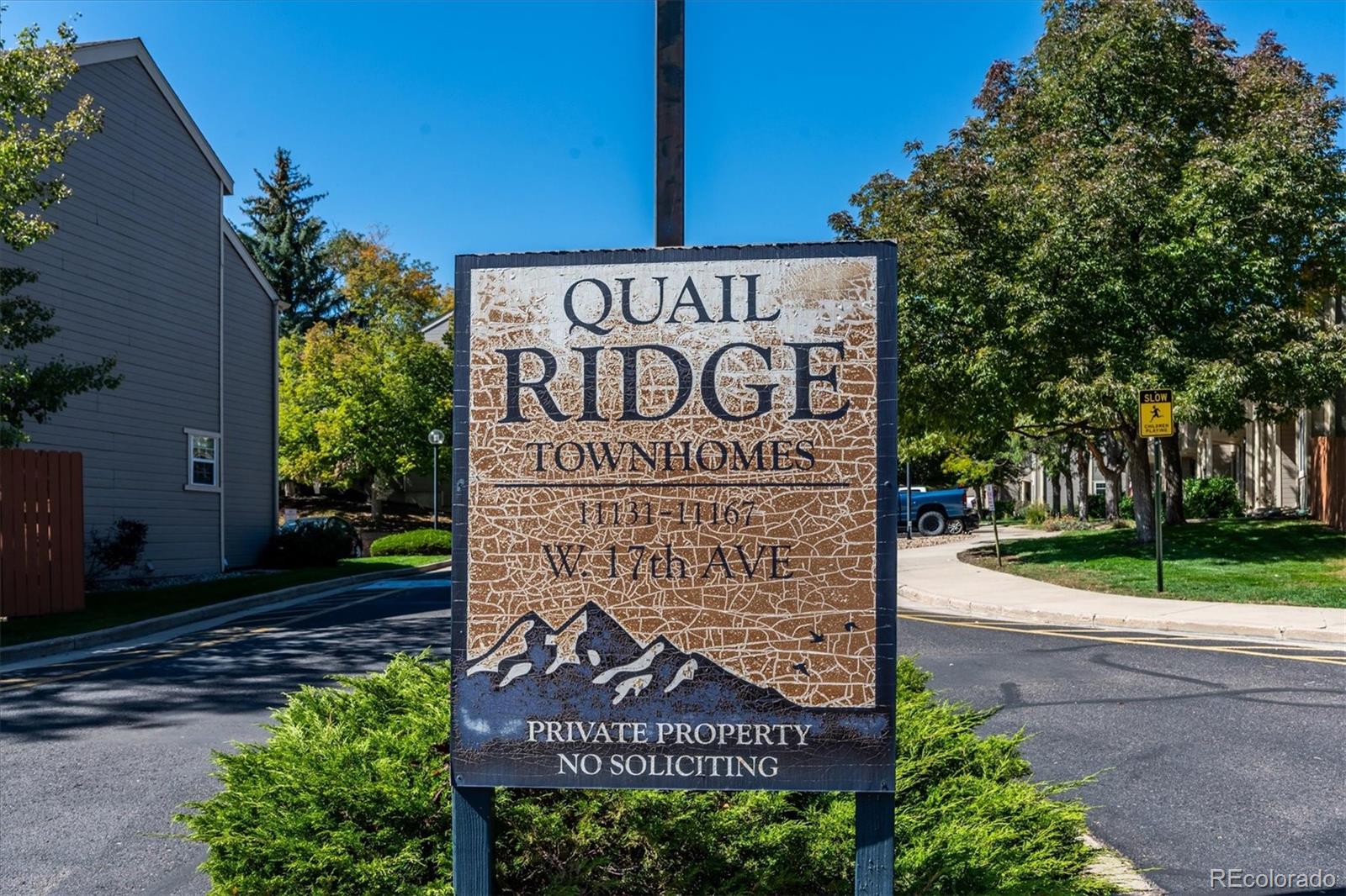 Quail Ridge Townhomes entrance sign beside the street, with townhomes and trees in the background.