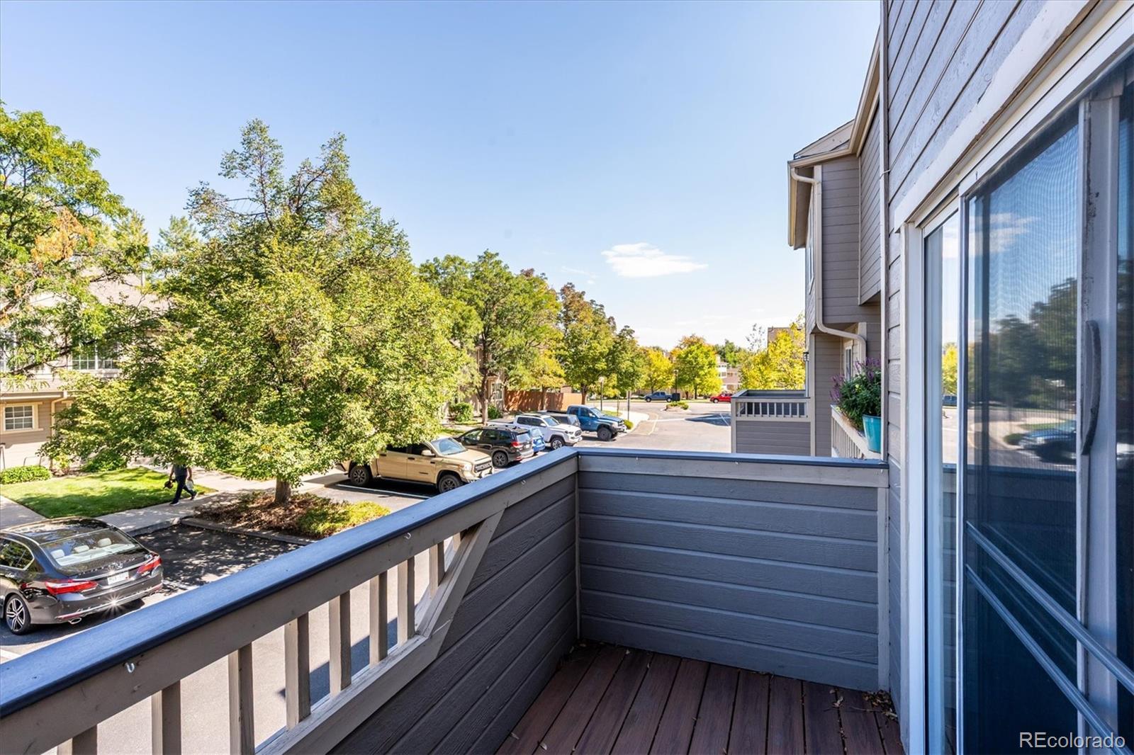 Condominium balcony overlooking a tree-lined parking area, with gray railings and dark wood decking.