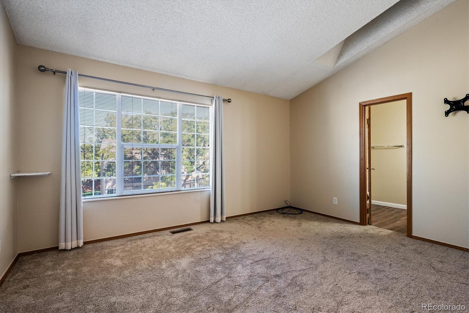 Vacant bedroom with beige carpet, a large curtained window, and a doorway to an adjoining room.