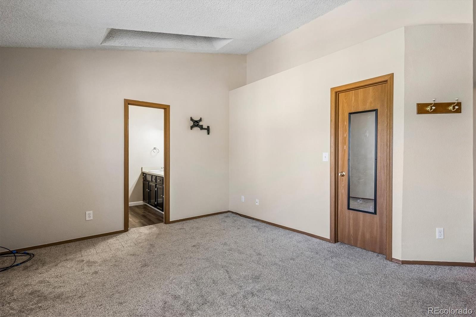 Empty carpeted room with a mirrored door and bathroom vanity visible through the doorway.