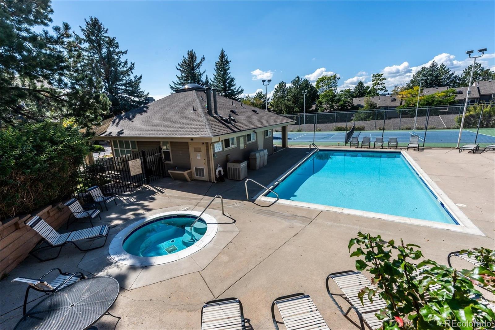 Community pool and hot tub beside a clubhouse, with tennis courts behind them.