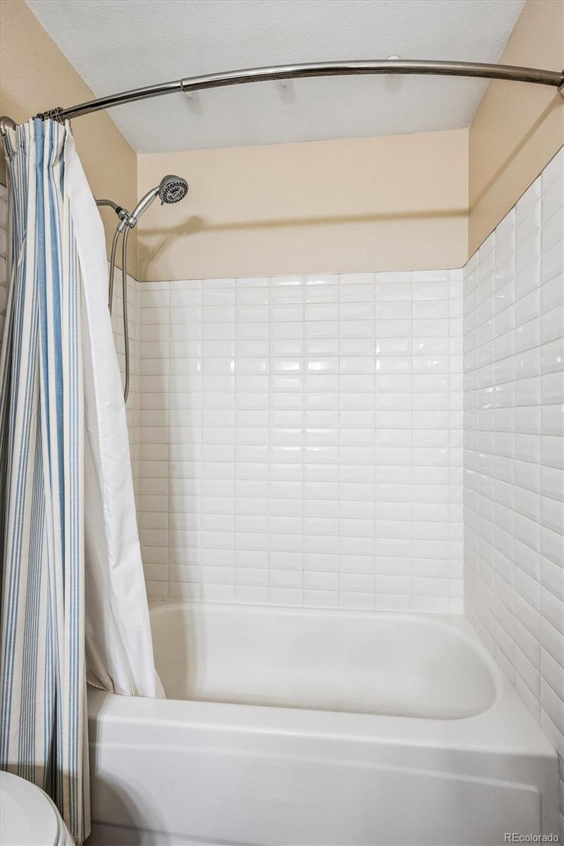 Bathroom bathtub and tiled shower with a handheld showerhead and striped curtain.