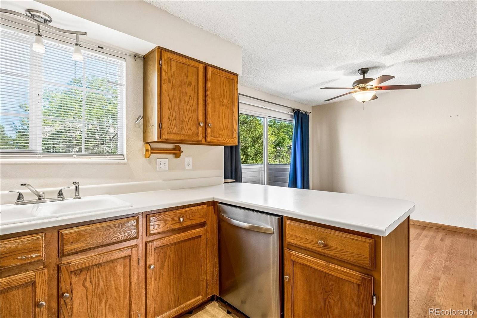 Kitchen with wood cabinets, white counters, stainless steel dishwasher, and sliding glass door to a balcony.
