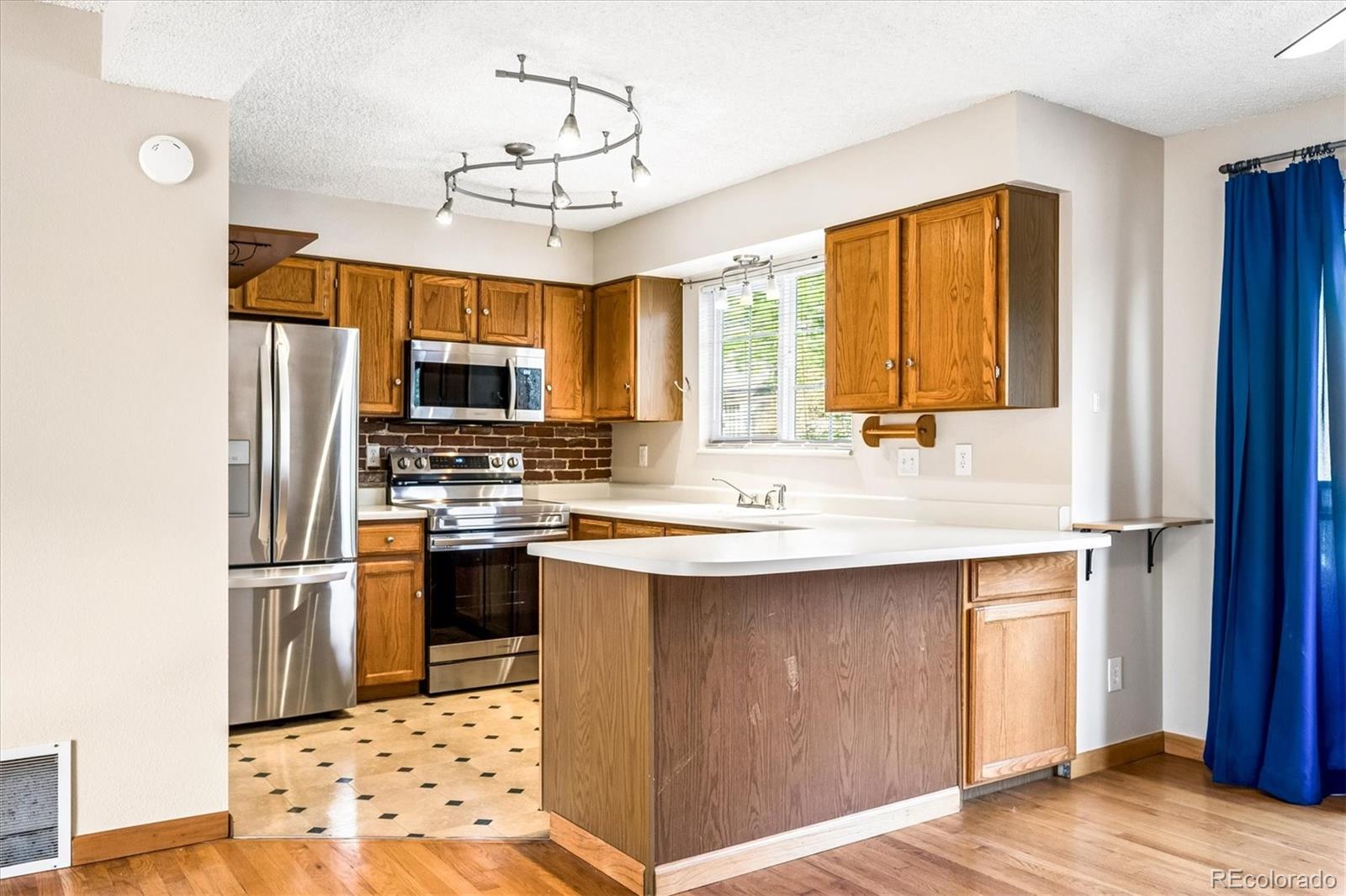Kitchen with wood cabinets, stainless steel appliances, a white peninsula, and brick backsplash.