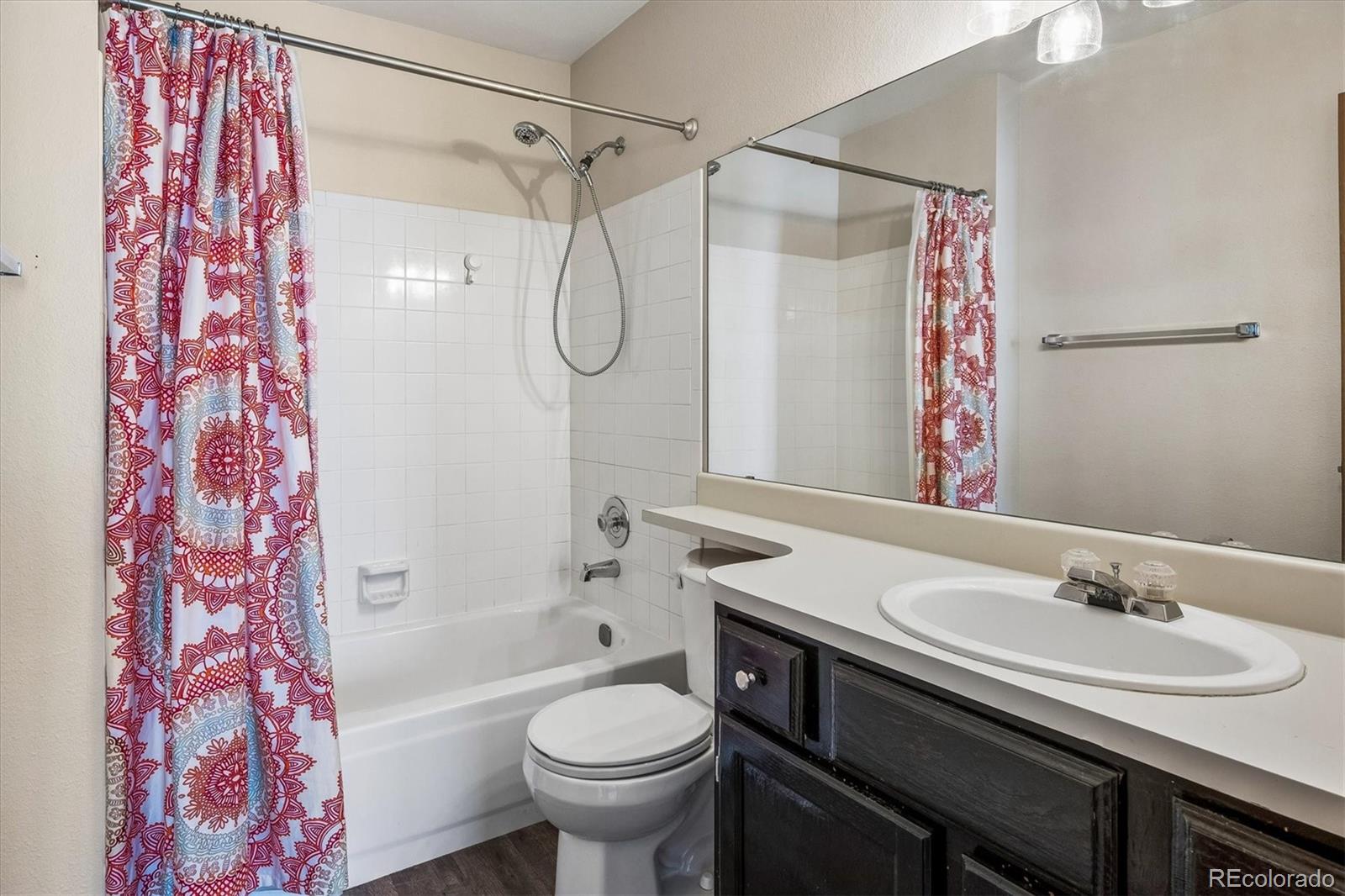 Bathroom with a tiled tub and shower, colorful patterned curtain, and dark wood vanity.