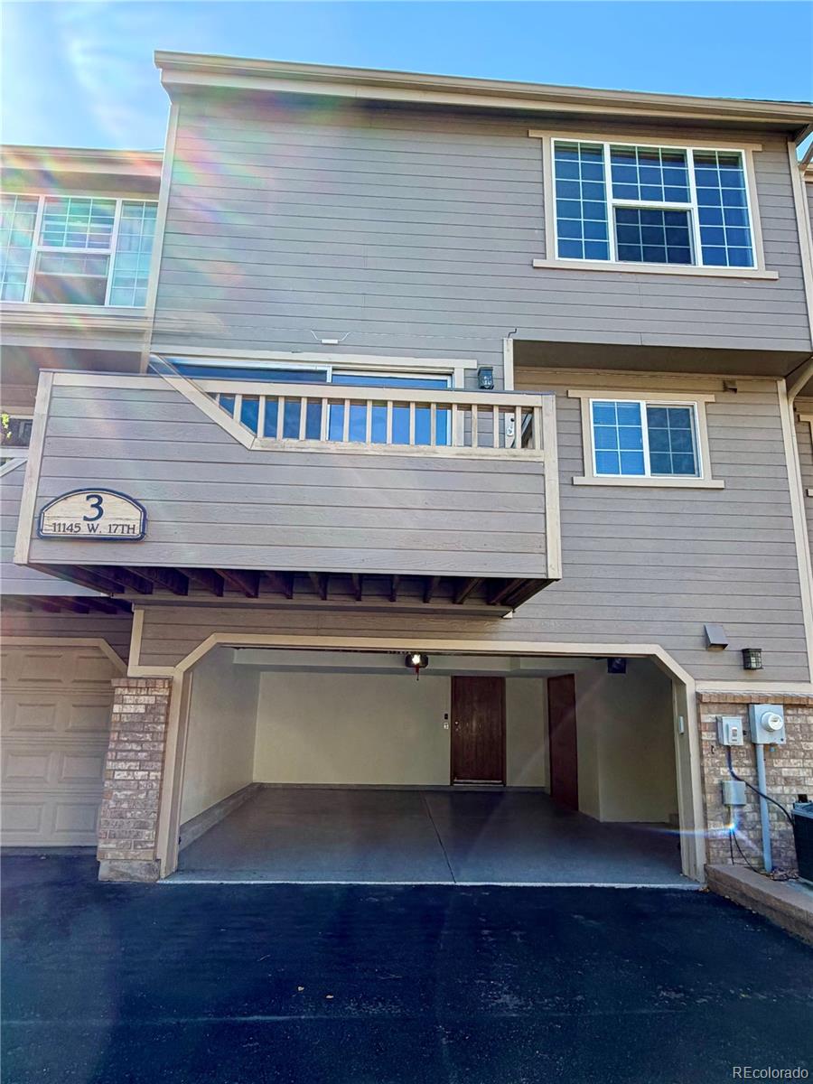 Gray townhouse exterior with a raised balcony and open garage beneath it.