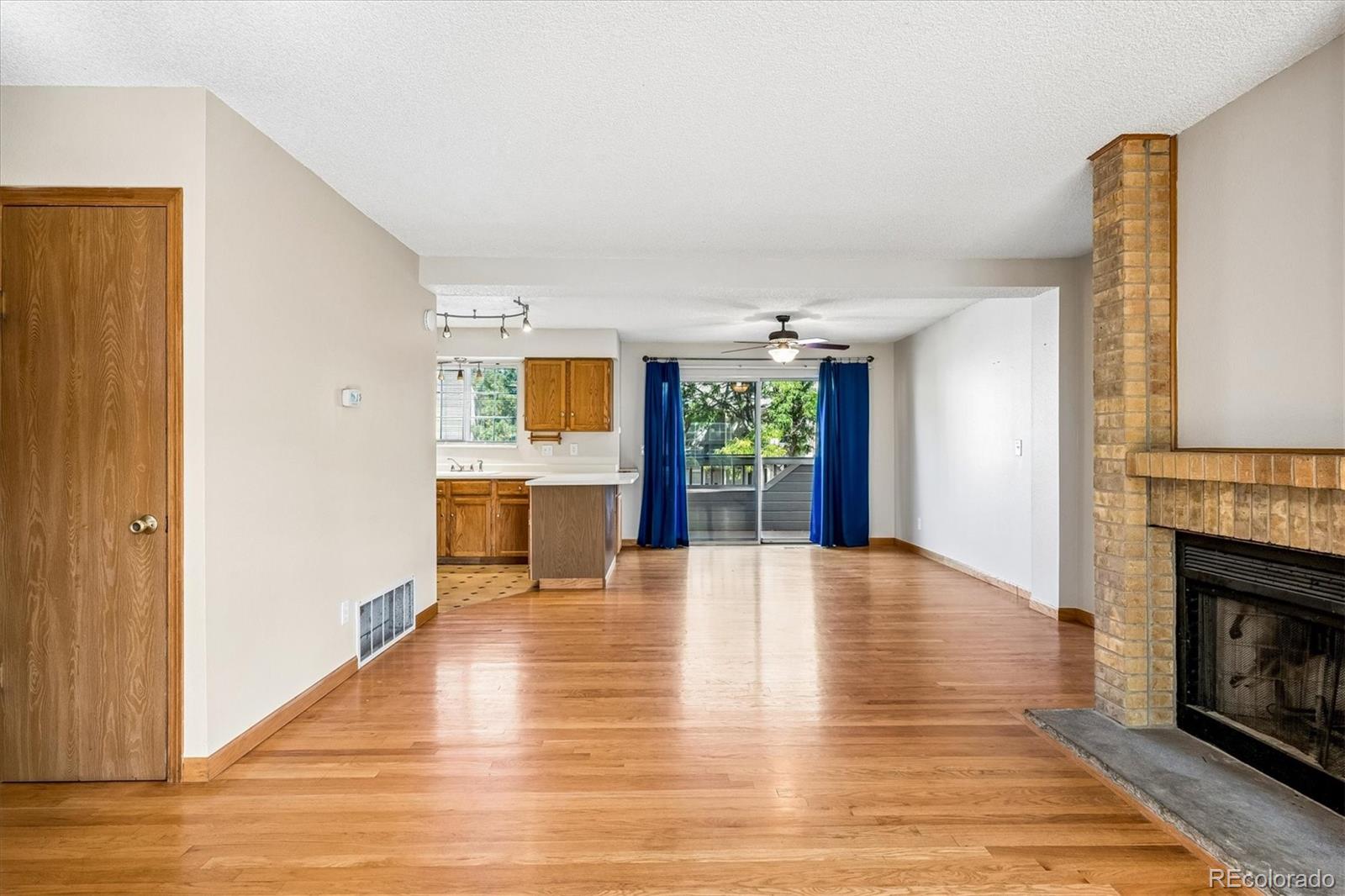 Unfurnished living room with hardwood floors, brick fireplace, open kitchen, and sliding doors to a deck.