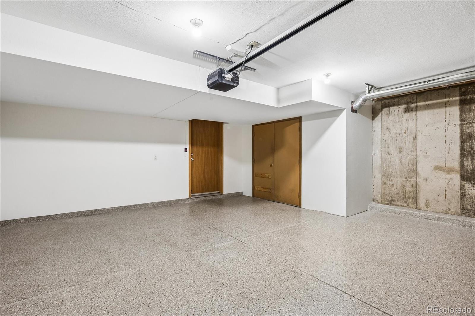 Vacant garage with a speckled concrete floor and ceiling-mounted door opener.