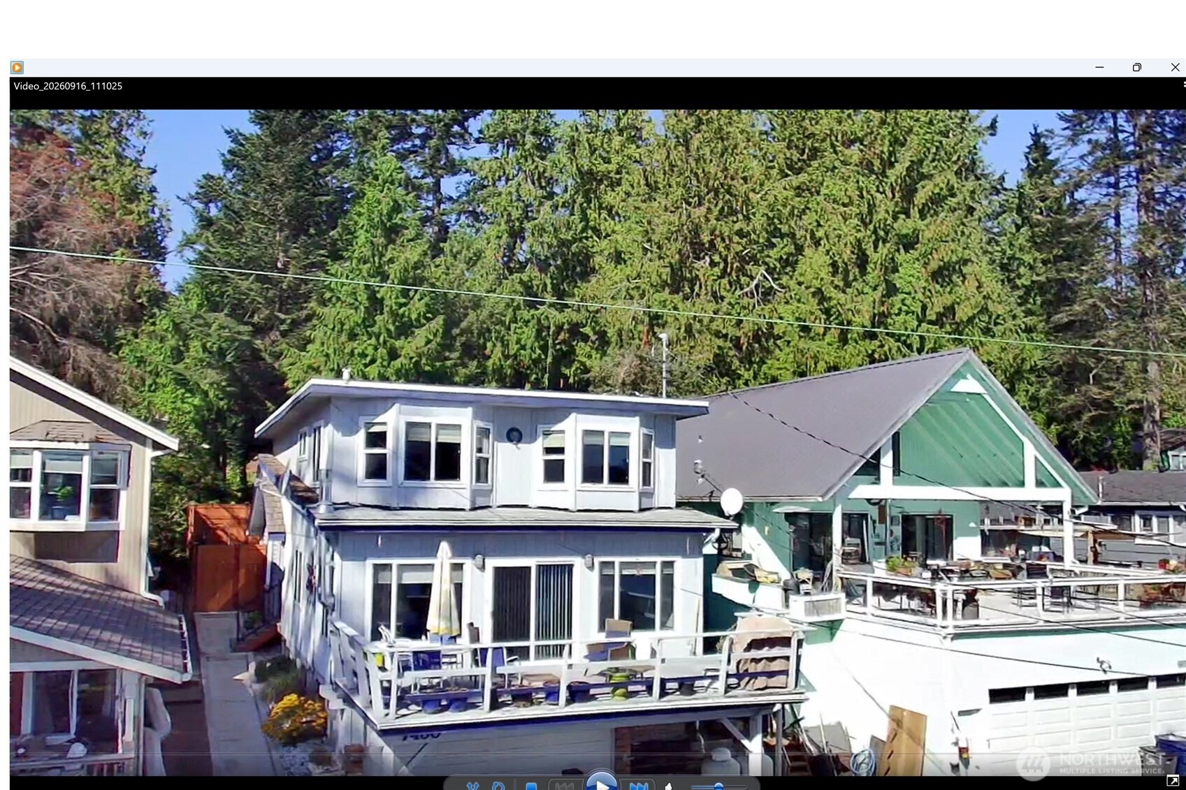 Two-story light-colored home with broad balconies beside a green gabled building.