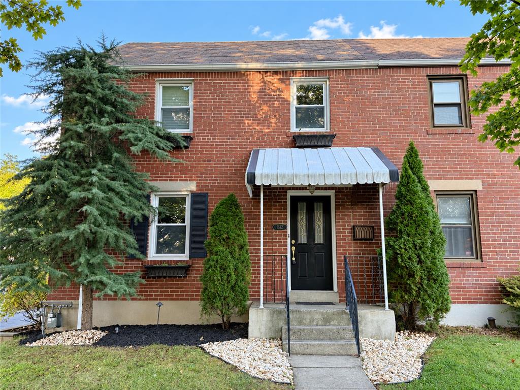Brick-front home with a white entrance awning, front steps, and landscaped shrubs.