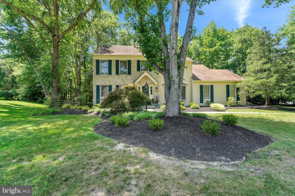 Two-story stone-and-siding home with green shutters, mature trees, and a landscaped front lawn.