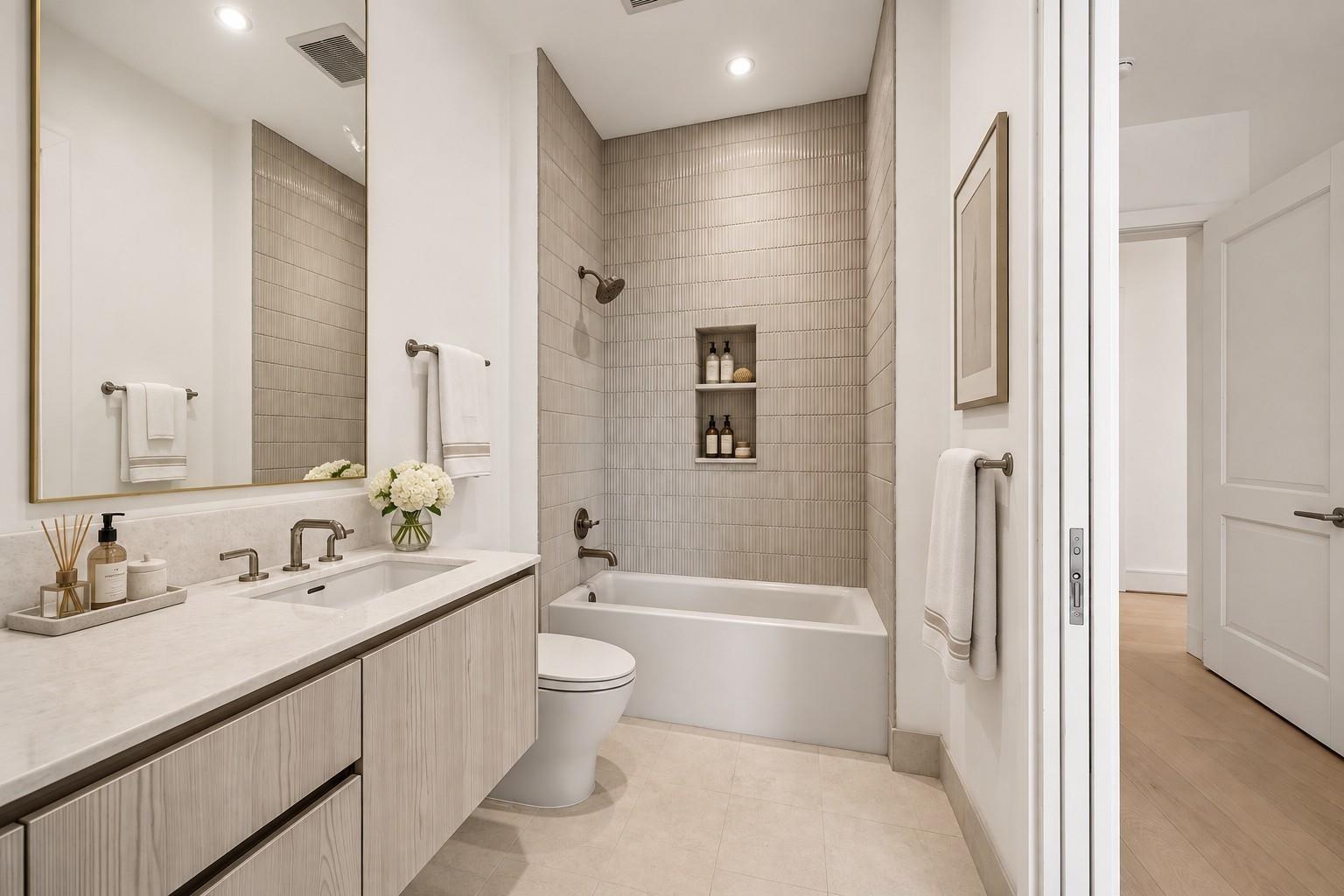 Modern bathroom with a pale wood vanity and tiled tub-shower with recessed shelves.