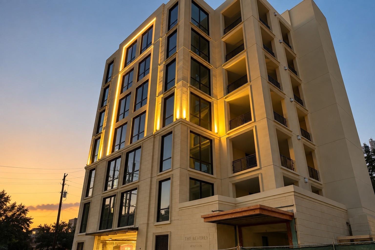Modern condominium building with illuminated facade, balconies, and The Beverly Houston entrance at dusk.