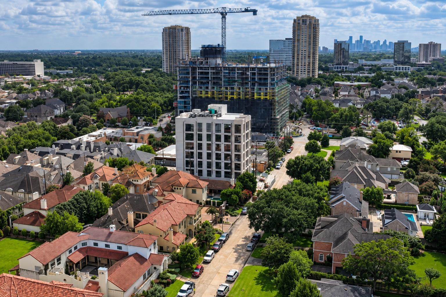 Aerial Houston view of a leafy neighborhood, a high-rise under construction, and the distant downtown skyline.