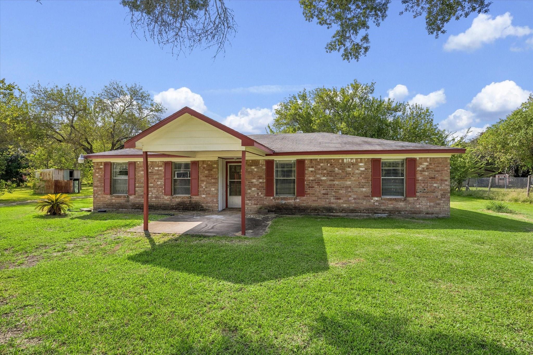 Single-story brick house with red shutters, a covered entry, and a broad green lawn.