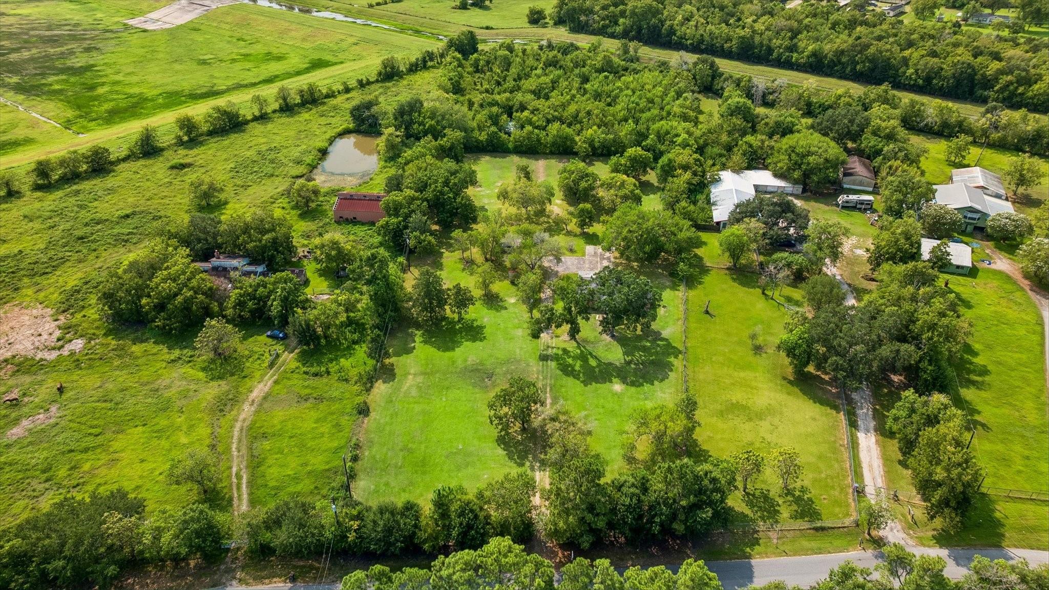 Aerial view of a tree-lined rural property with several buildings and a small pond.