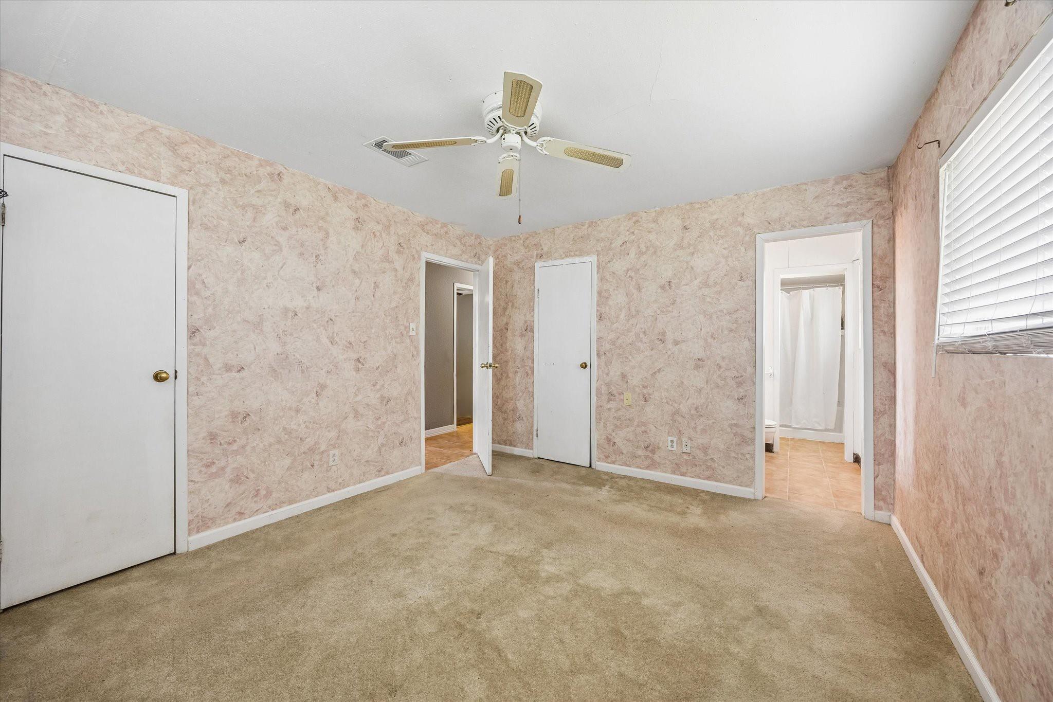 Empty bedroom with beige carpet, pink textured walls, and a ceiling fan.