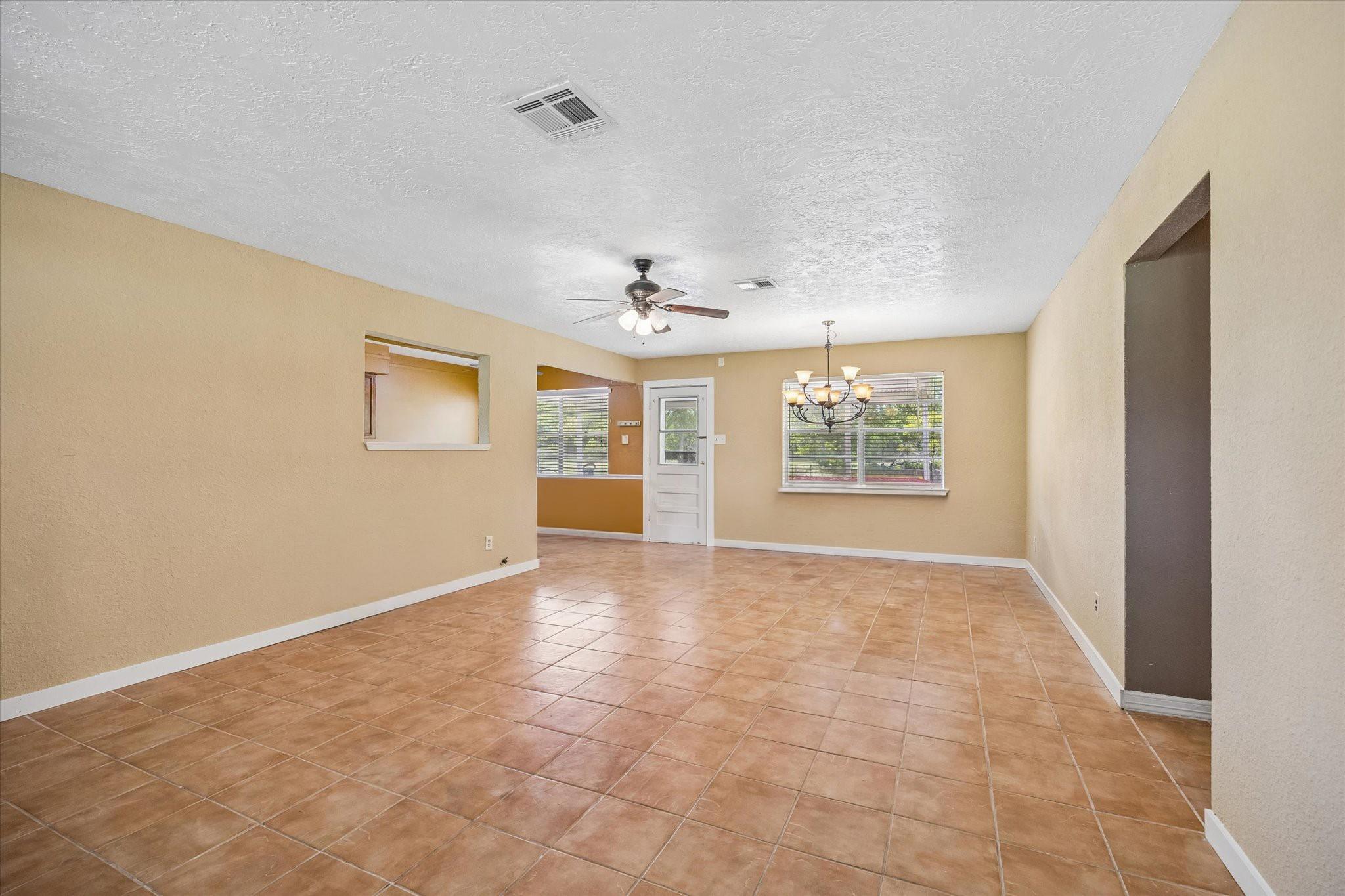 Empty tiled living area with tan walls, a ceiling fan, and a chandelier.