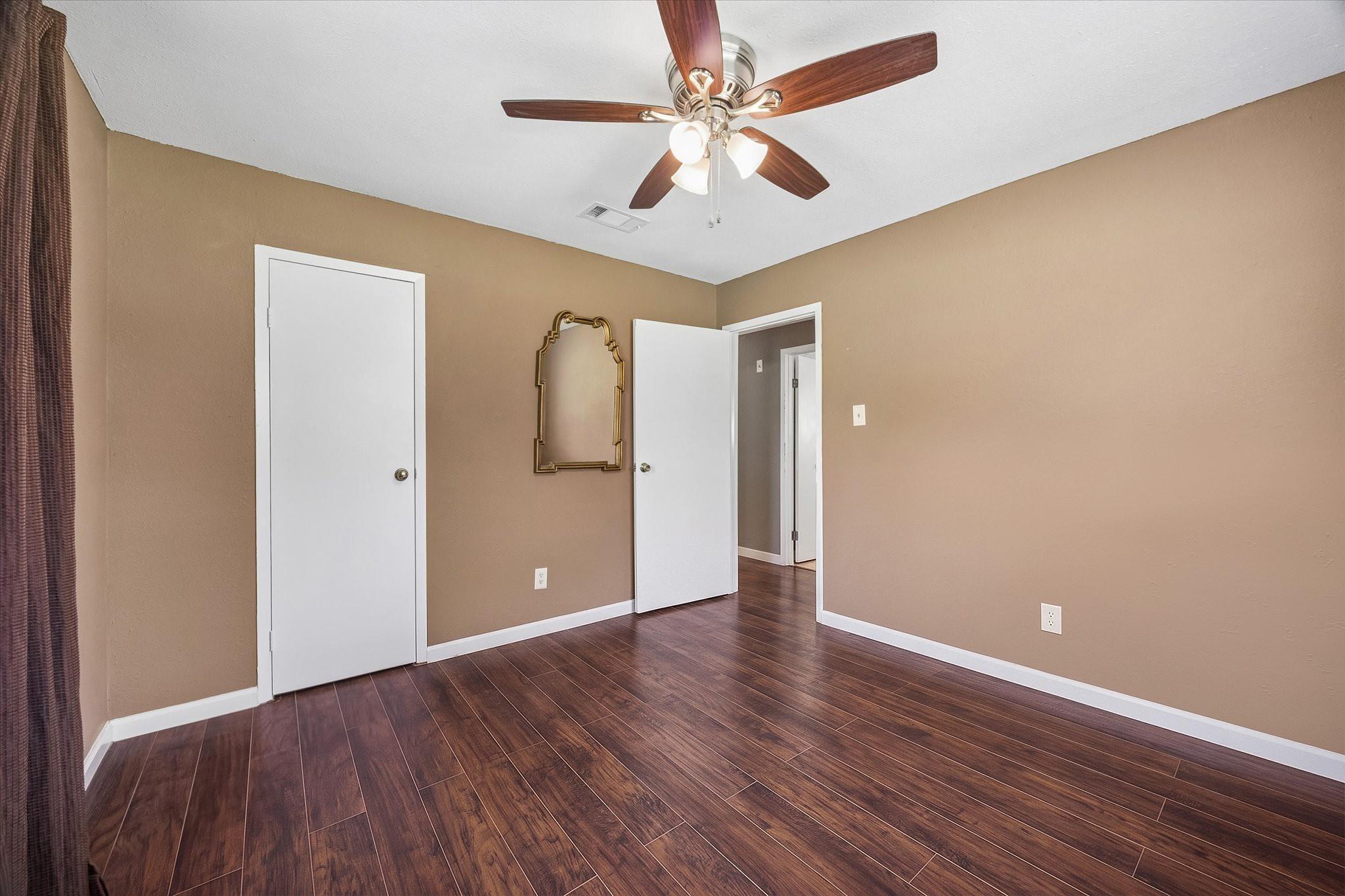 Empty room with dark plank flooring, tan walls, and a ceiling fan with lights.