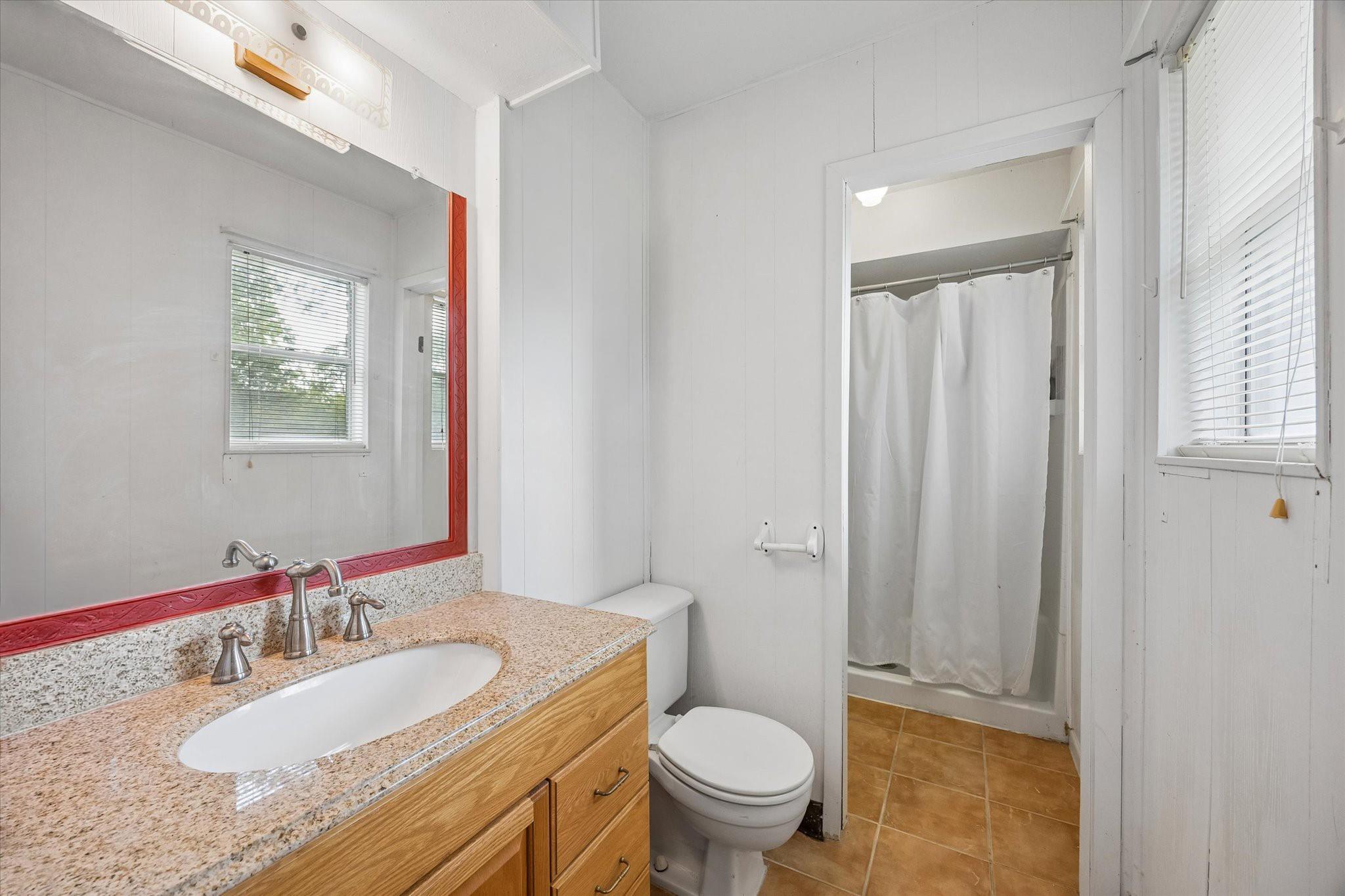 Bathroom with a granite vanity, red-trimmed mirror, toilet, and curtained shower.