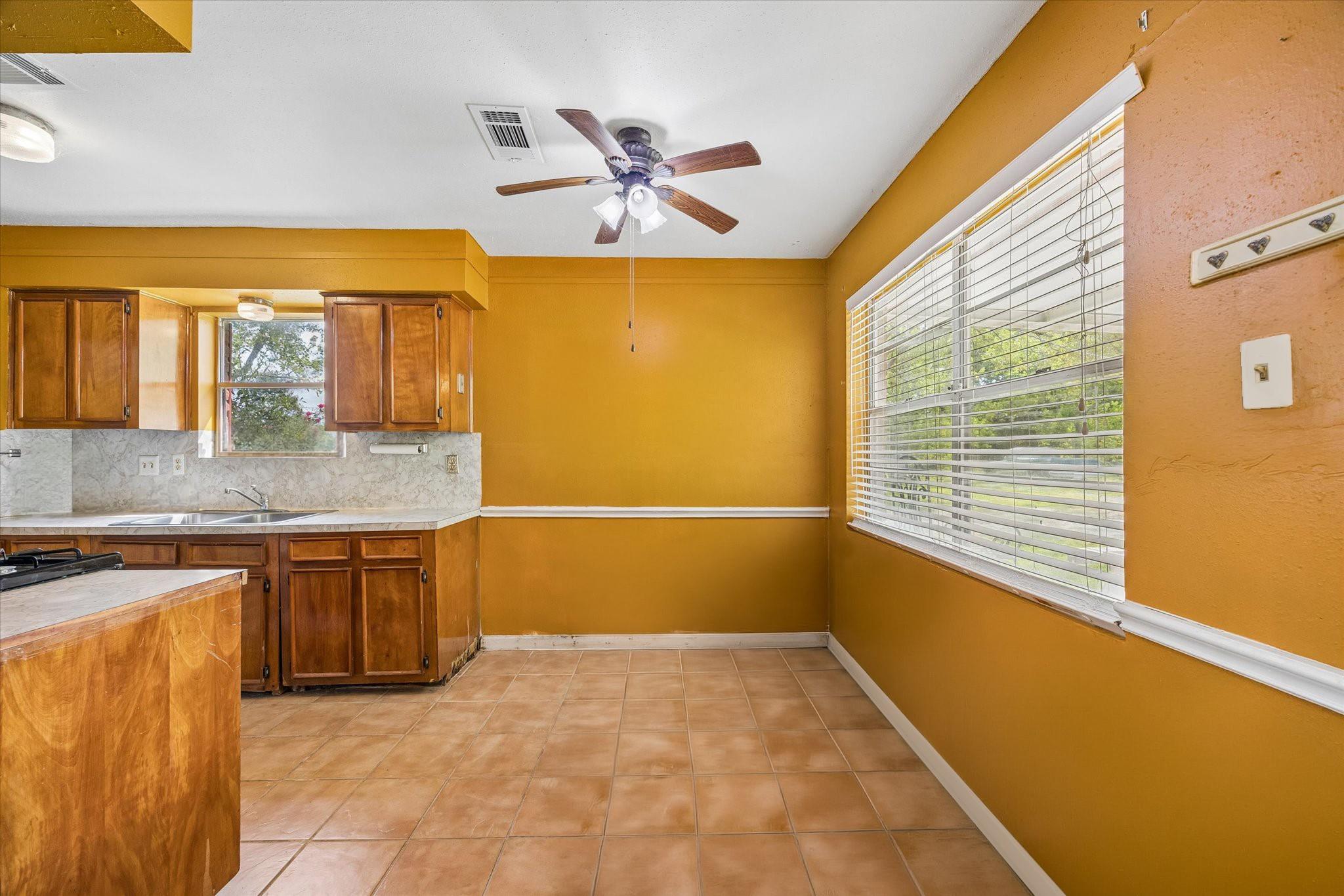 Kitchen with wood cabinets, terracotta tile floor, mustard-yellow walls, and a wide window with blinds.