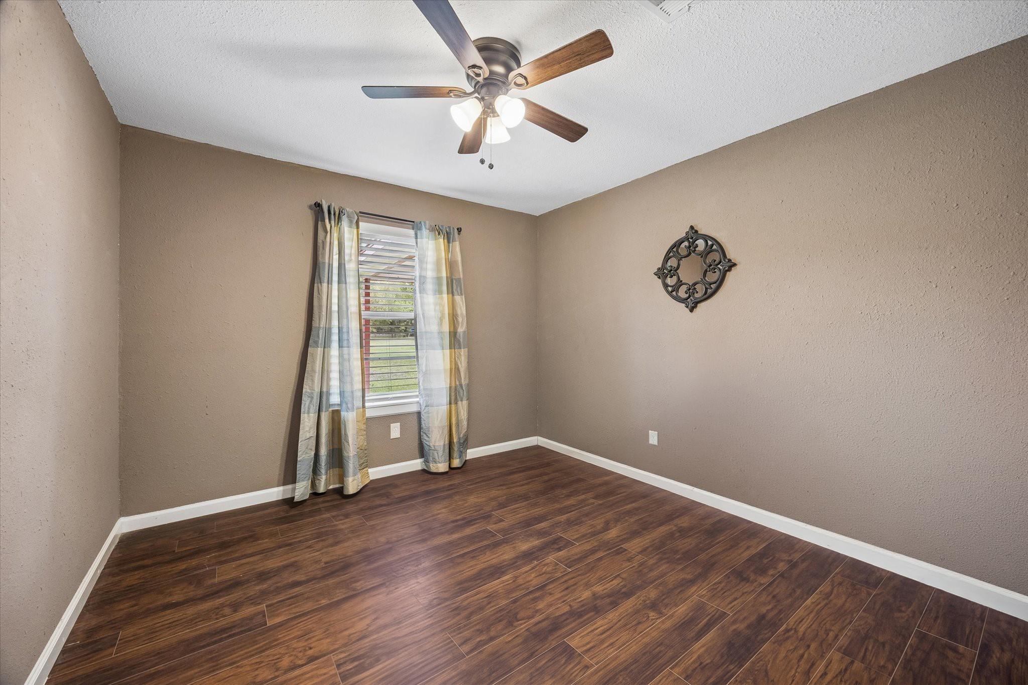 Empty bedroom with dark wood-look flooring, striped curtains, and a ceiling fan.