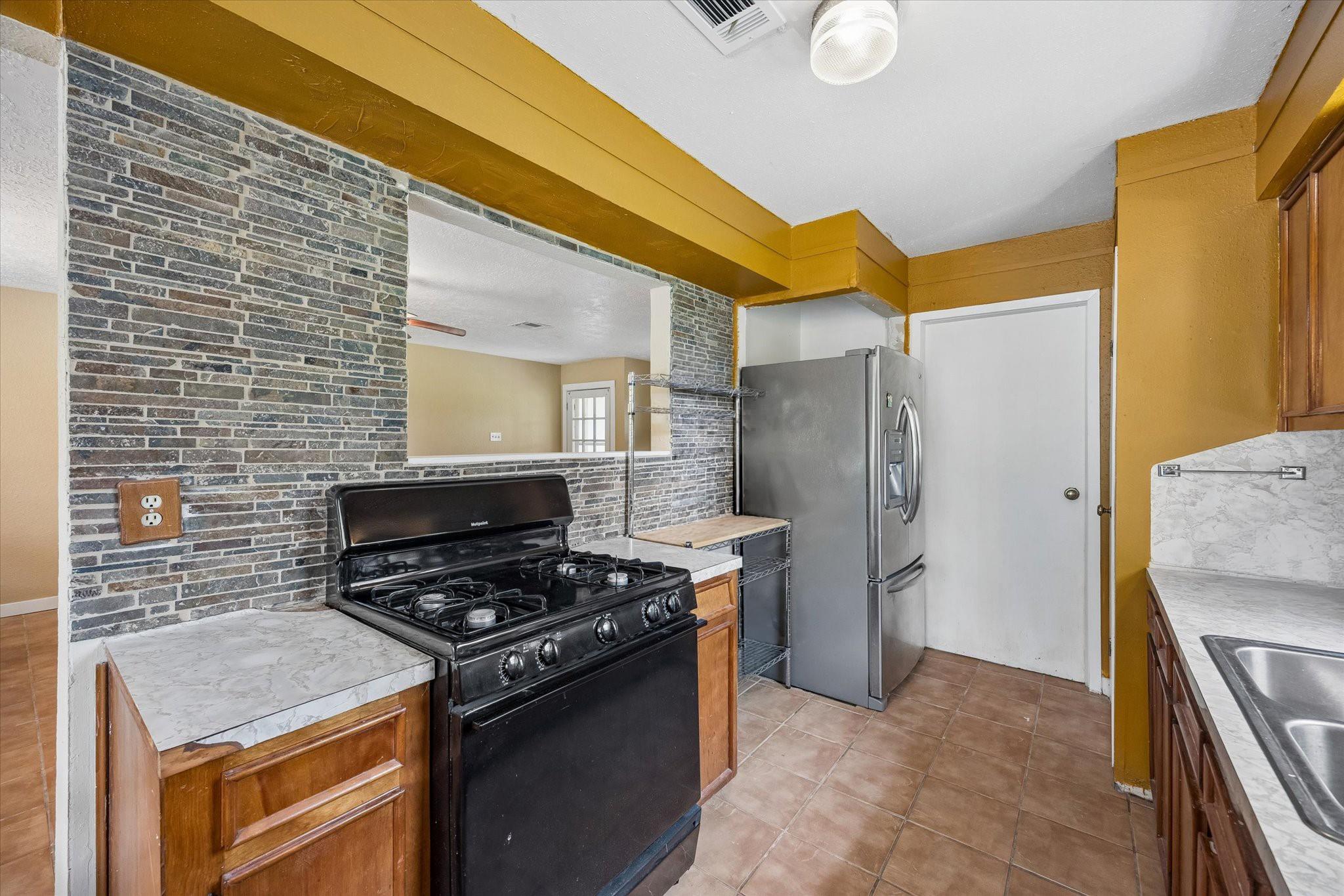 Kitchen with a black gas range, stainless refrigerator, gray brick backsplash, and marble-pattern counters.