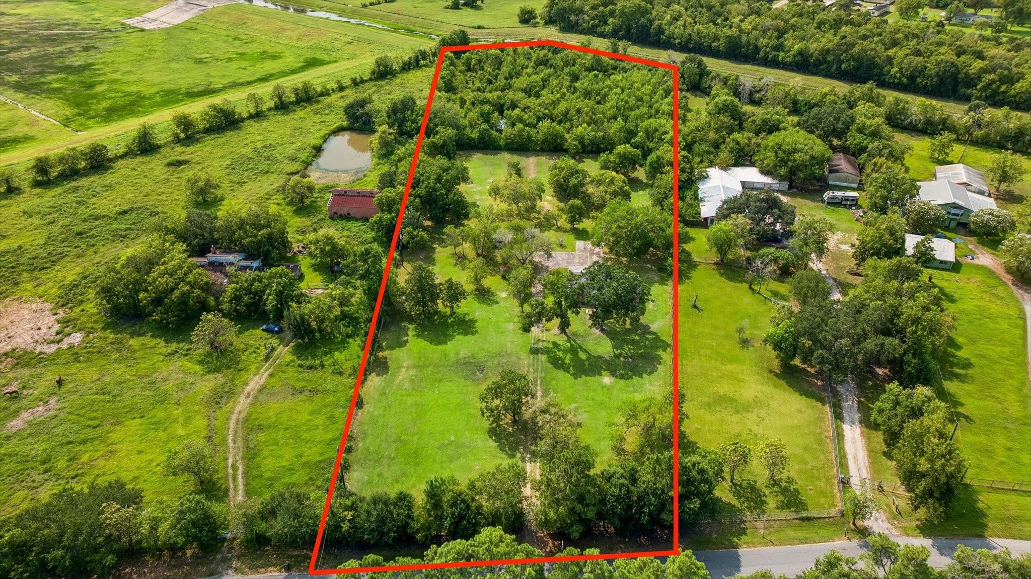 Aerial view of a tree-shaded rural property outlined in red, with a broad lawn and paved area.