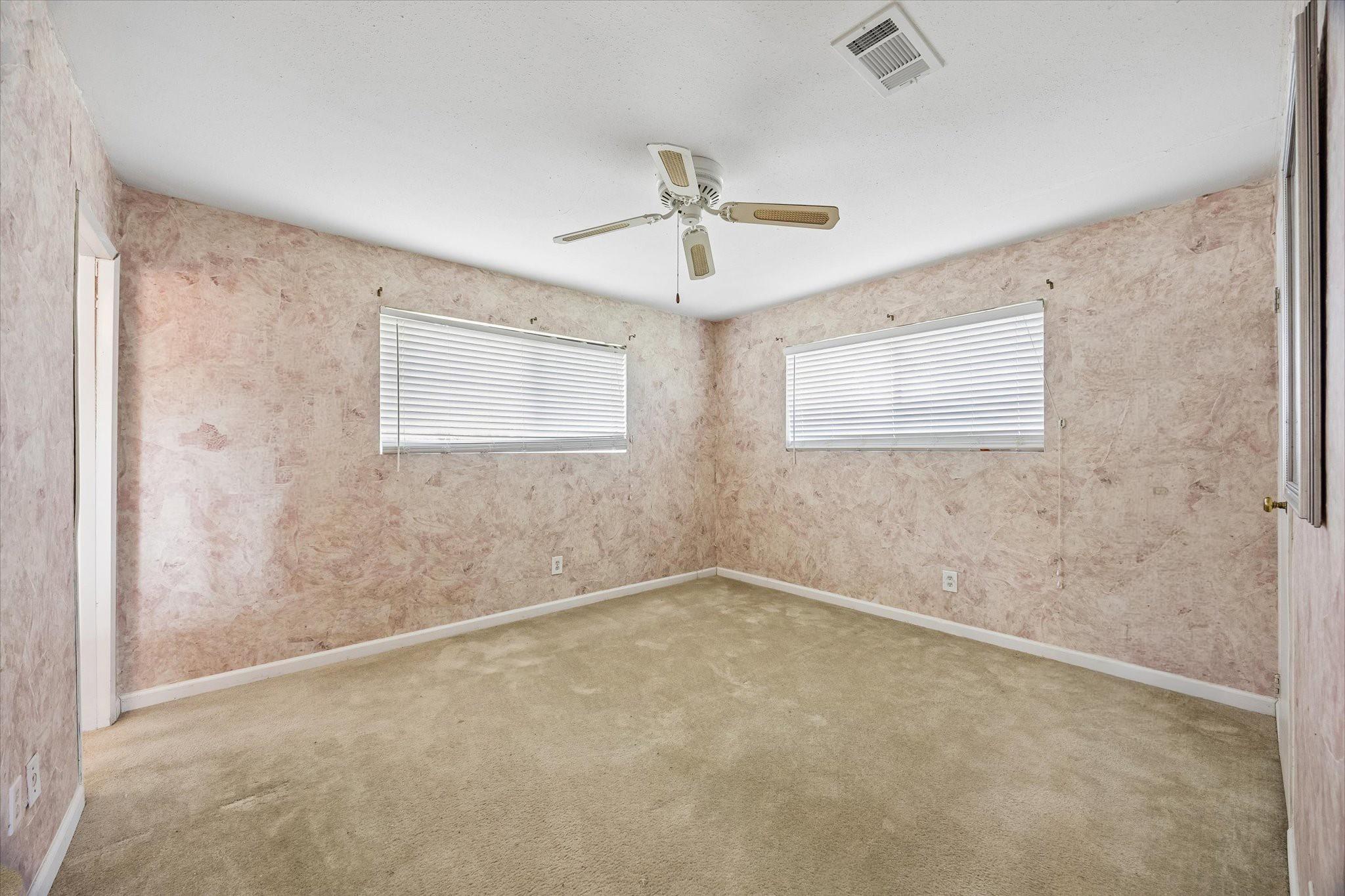 Empty bedroom with beige carpet, two blinded windows, and a ceiling fan.