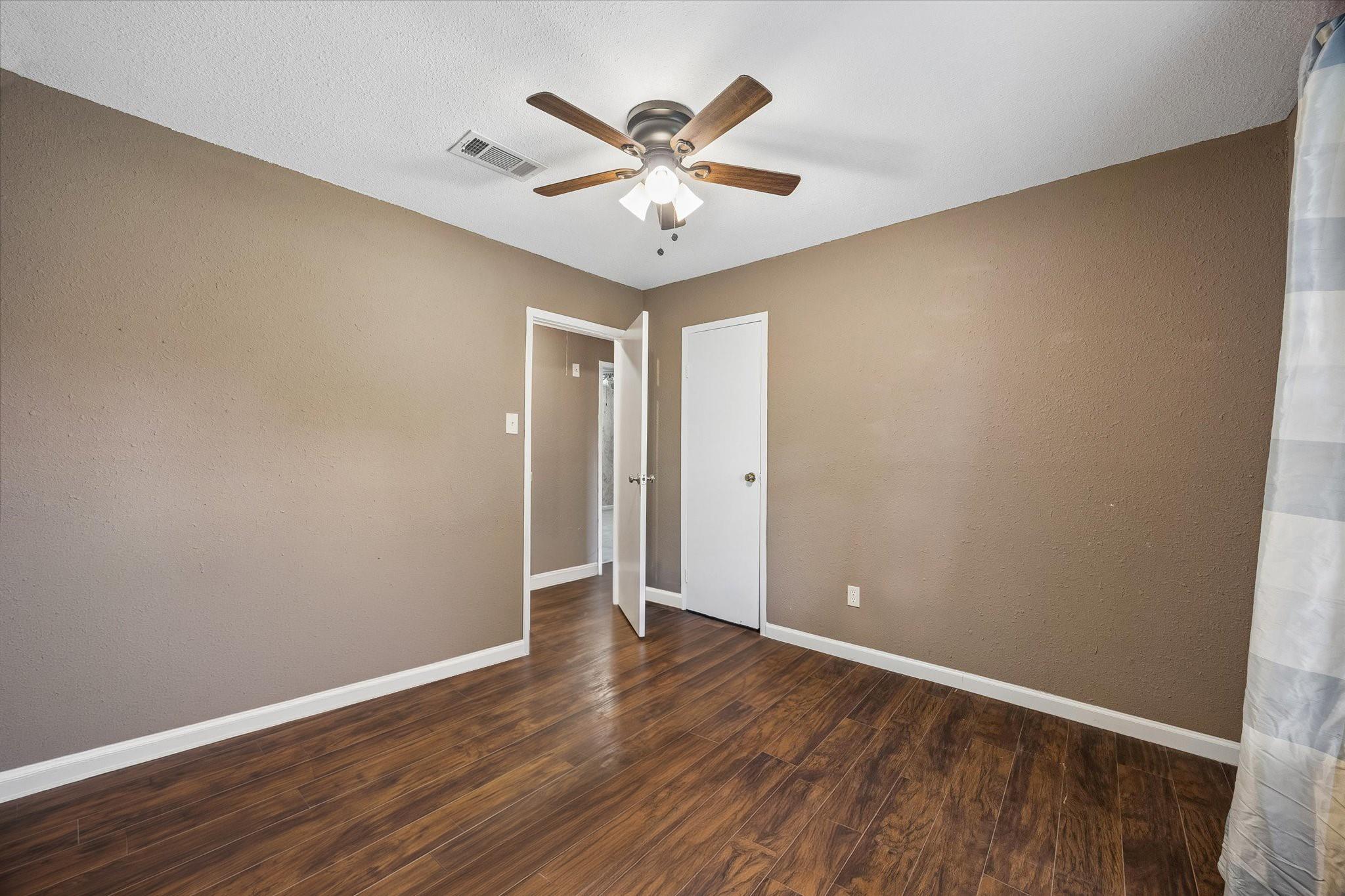 Empty bedroom with dark wood-look flooring, a ceiling fan, and a curtained window.