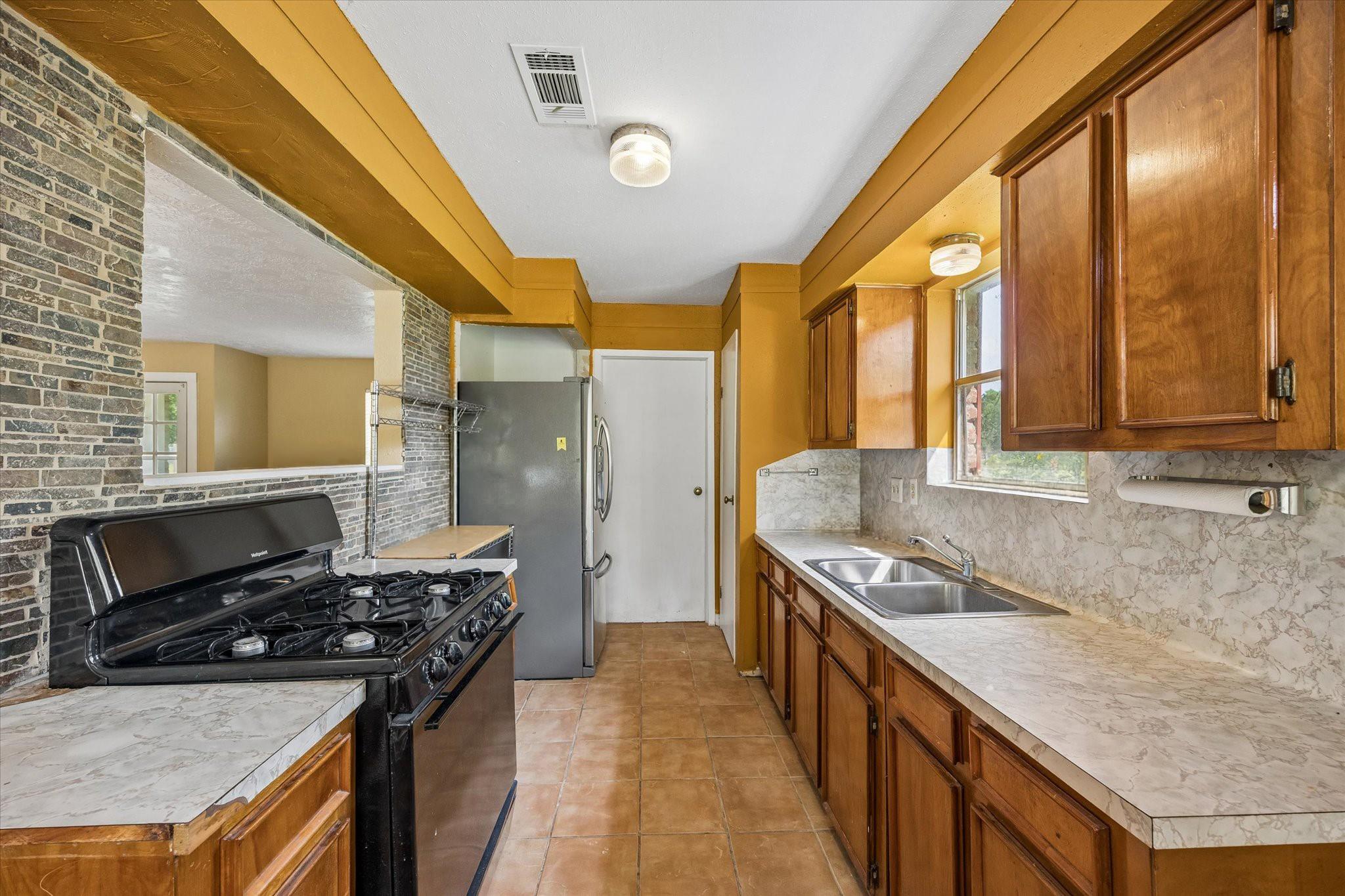 Kitchen with warm wood cabinets, marble-look counters, a double sink, and a black gas range.