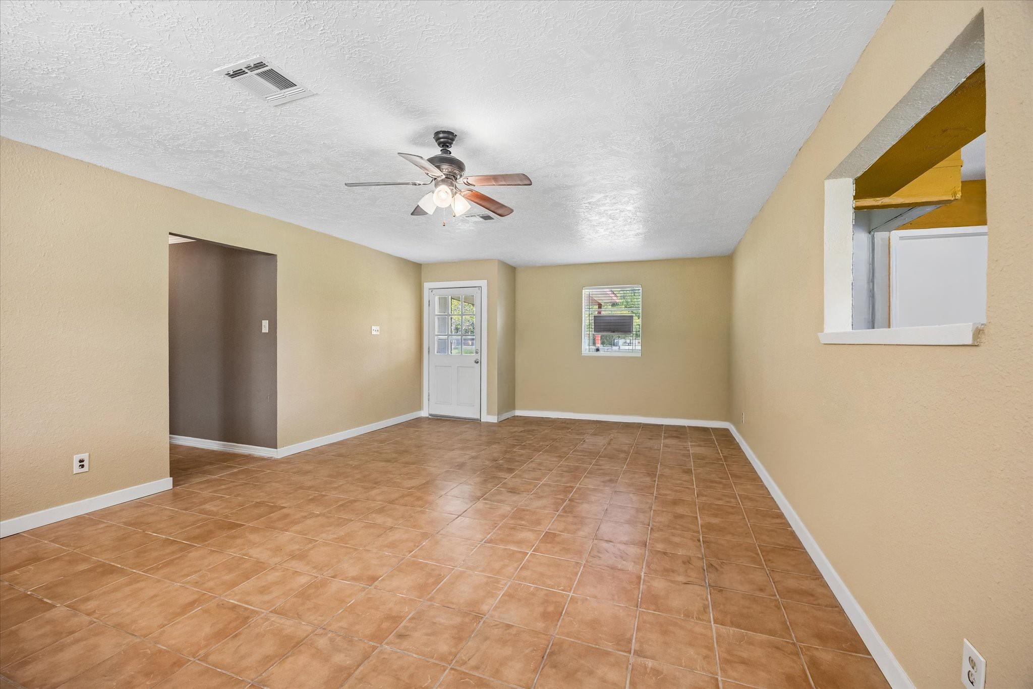 Empty room with terracotta tile floors, tan walls, ceiling fan, and a white door.