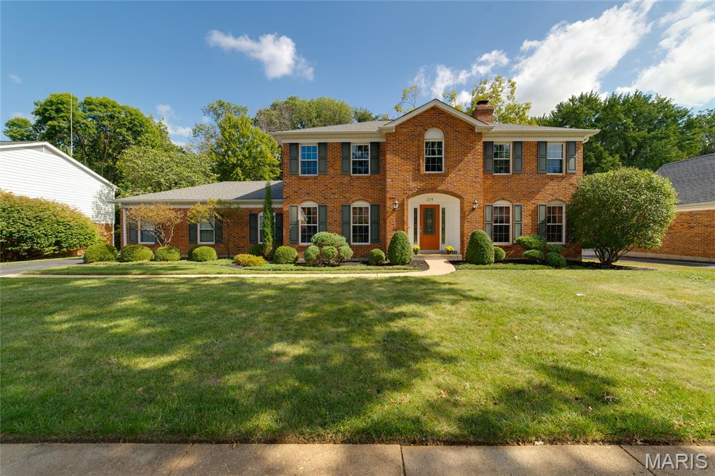 Two-story brick house with an arched entrance, landscaped shrubs, and a broad front lawn.