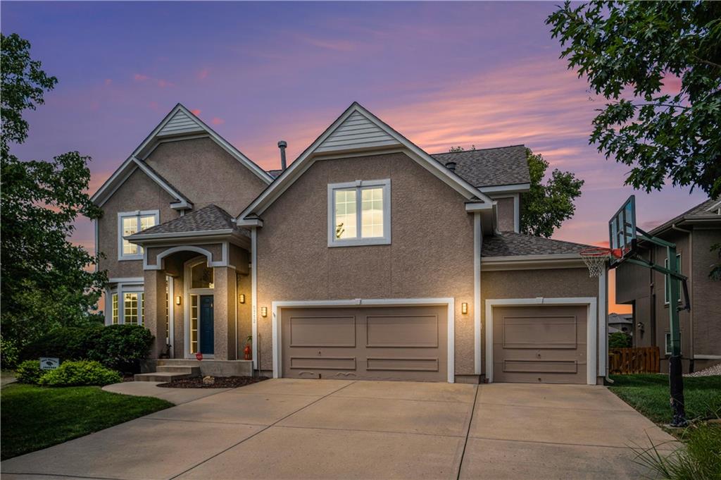 Two-story home with three-car garage and a basketball hoop beside the driveway at dusk.