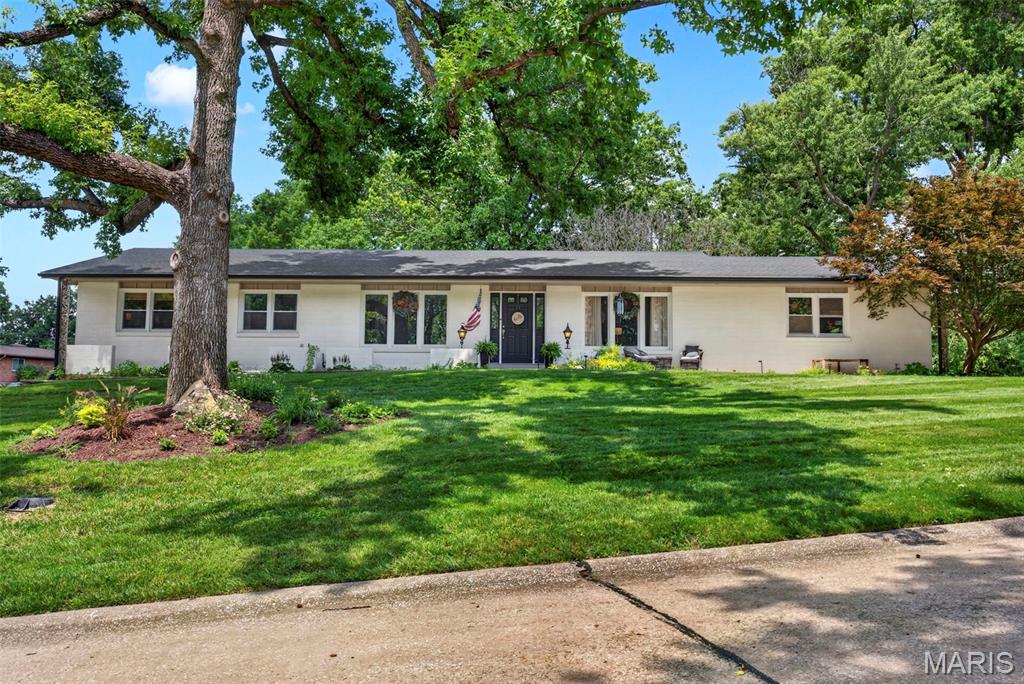 Single-story white house with a broad lawn and mature shade trees.
