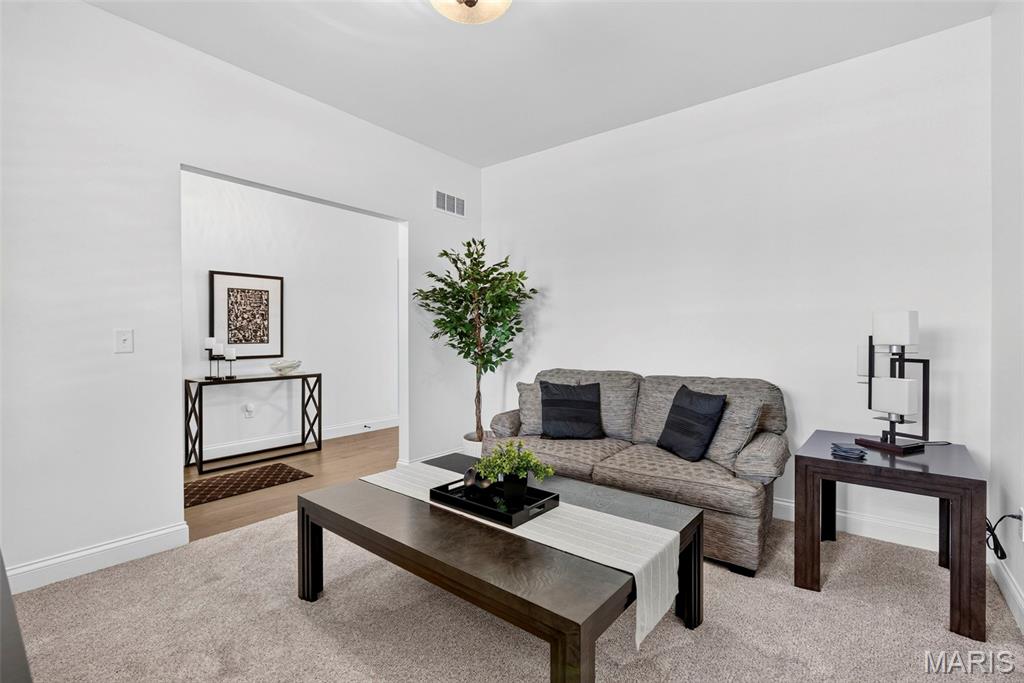 Staged living room with a gray sofa, dark wood coffee table, and neutral carpet.