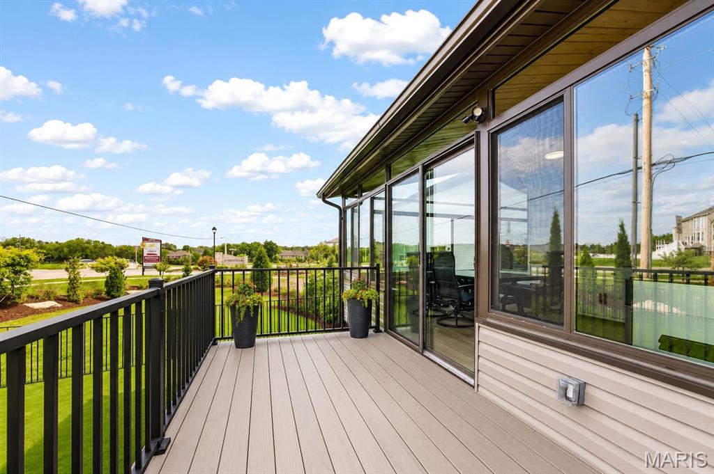 Raised deck with black railings beside a glass-walled room, overlooking a green lawn.