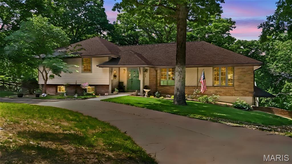 House with brick and light siding, a large front-yard tree, curved driveway, and American flag.